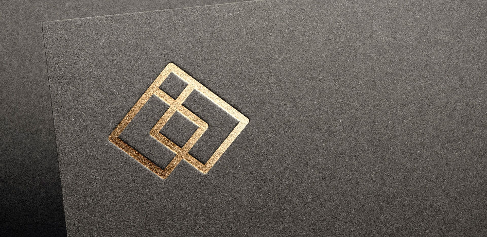 Gold foil embossed logomark on a textured gray paper.