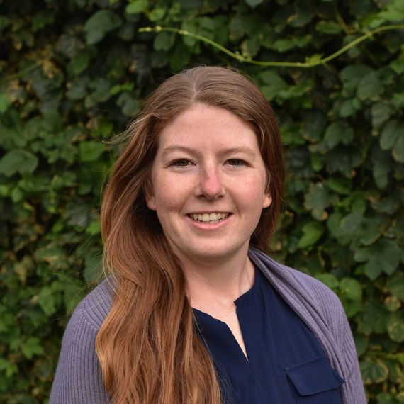 Renee, a creative designer based in Portland, OR standing in front of a wall of green ivy.