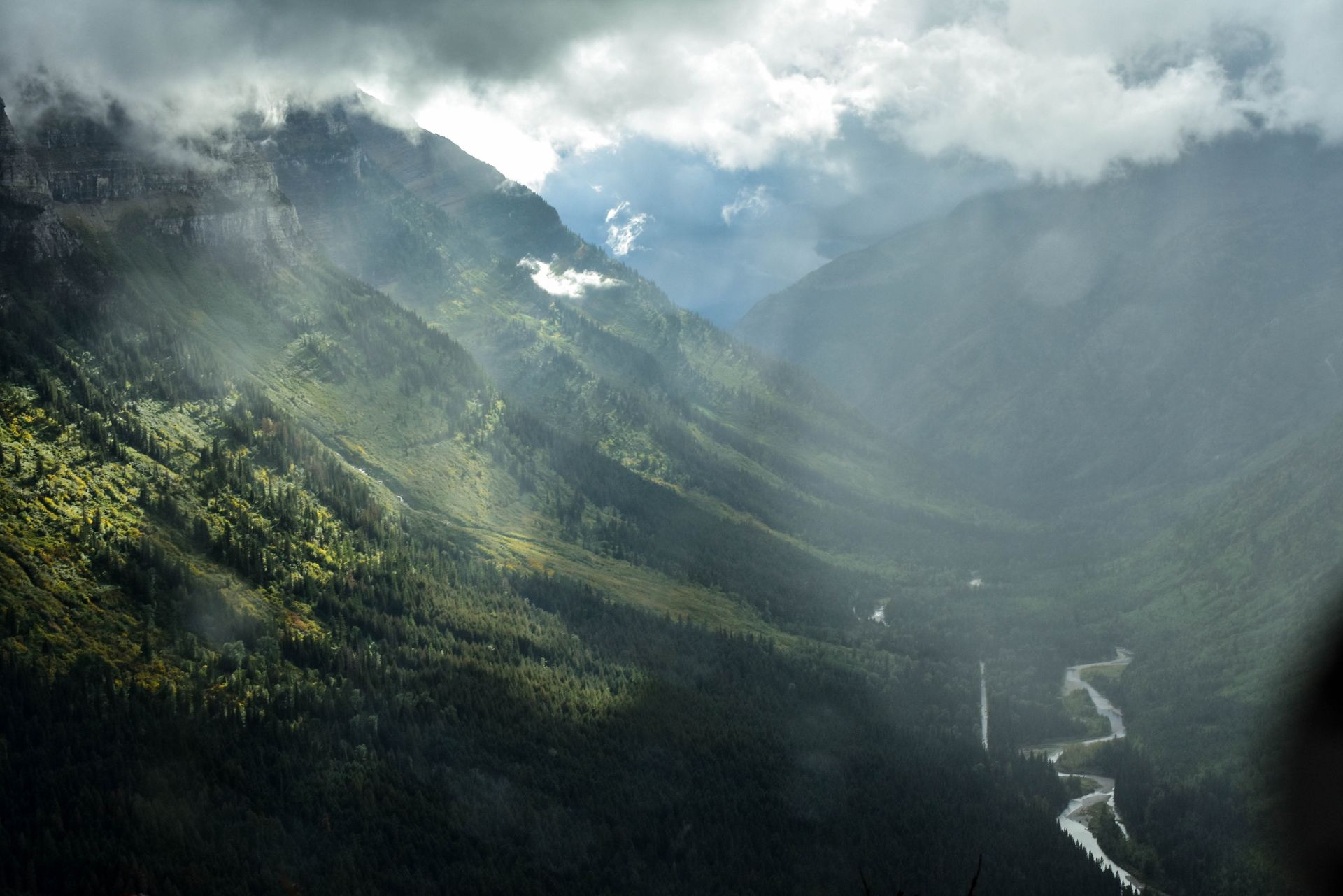 valley of green lit up by rays of sun coming through the gray clouds above