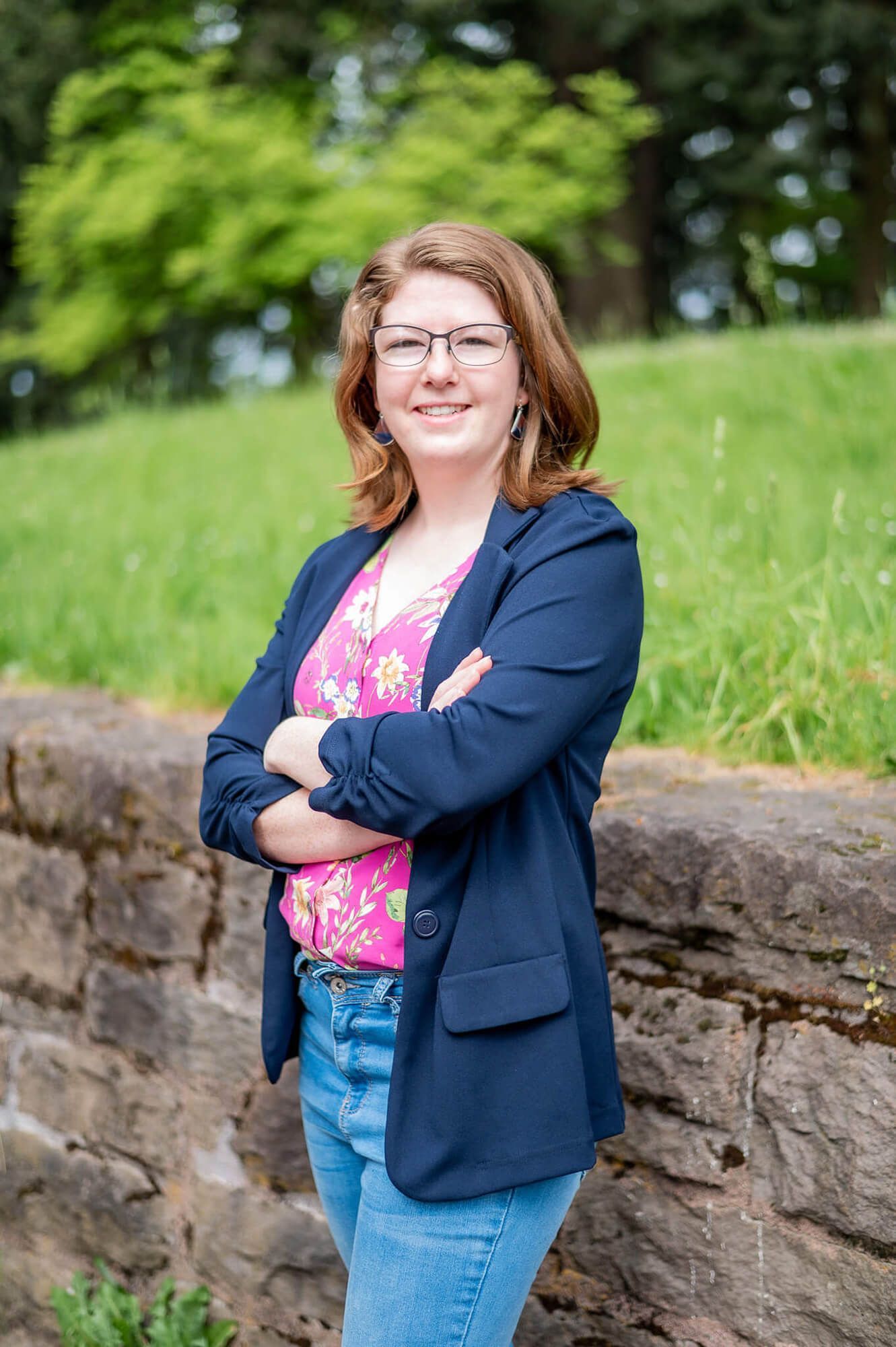 Photo of Renee, smiling, arms crossed. She is wearing a floral patterned shirt with a navy blue blazer.