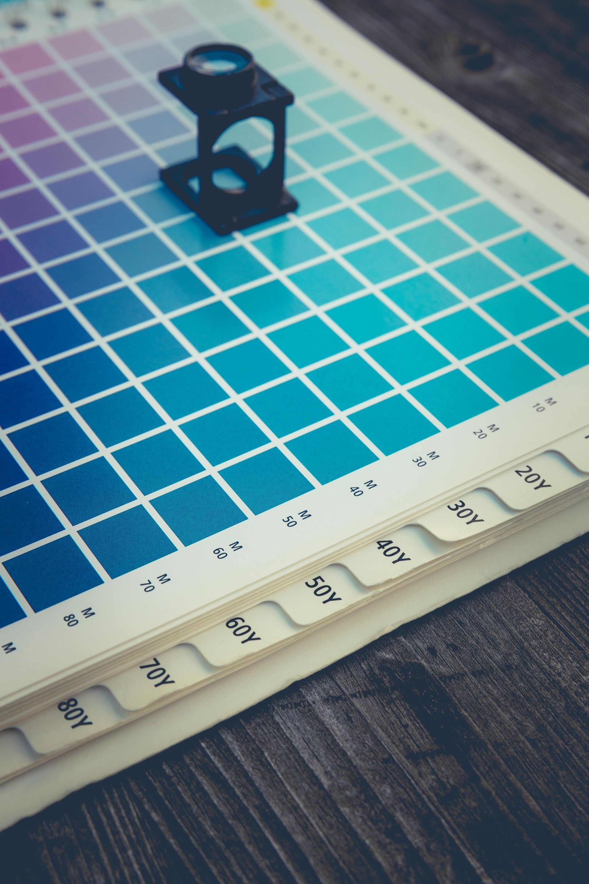 Printer’s loupe magnifier tool sitting on a paper with a gradient of cool colored boxes