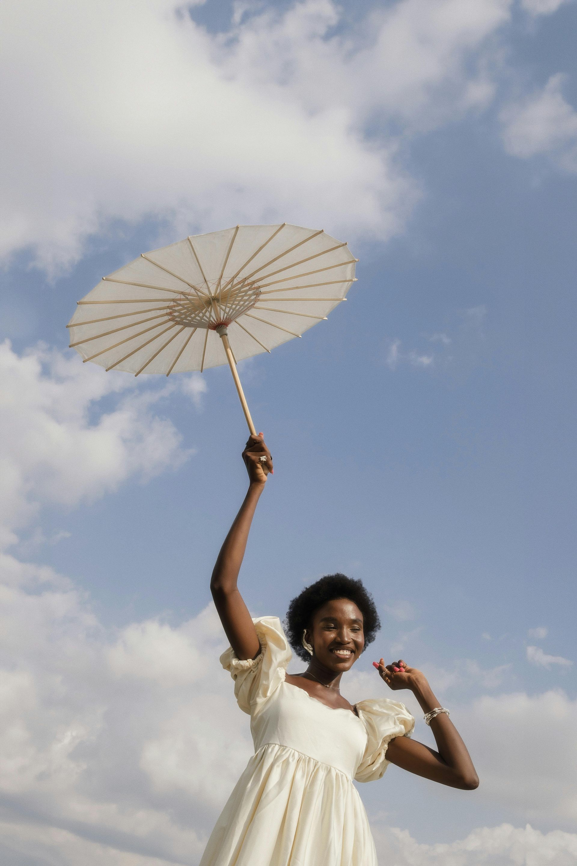 A joyful black woman holding an umbrella under a gorgeous blue and cloud filled sky