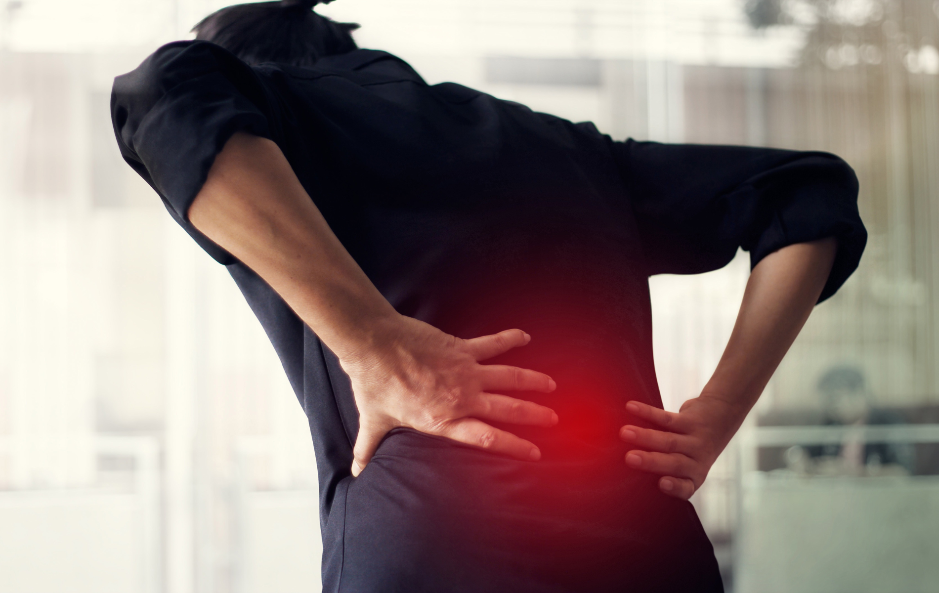 Person in black shirt holding their lower back, indicating pain; red glow highlights the area.