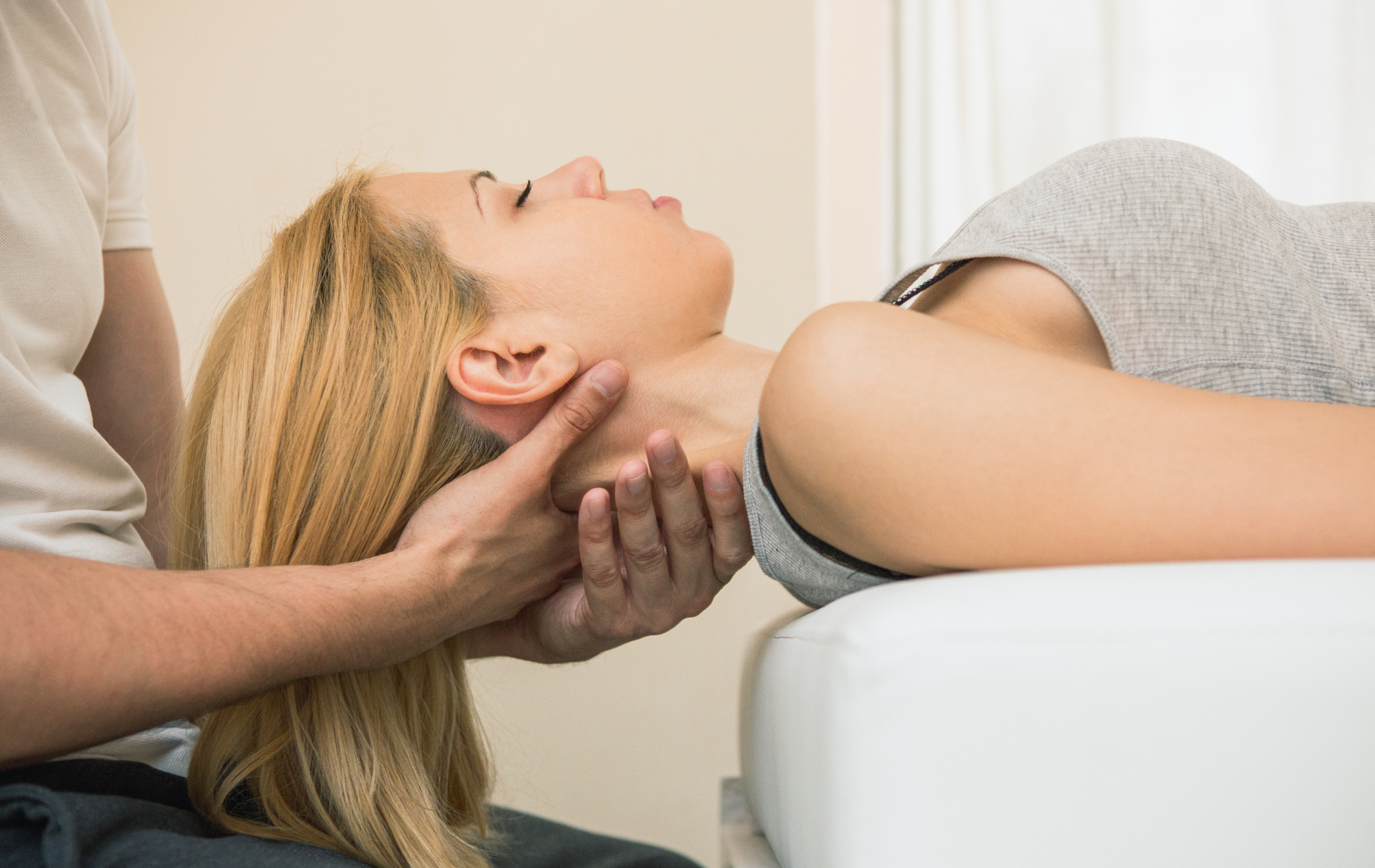 A person receiving neck adjustment. A healthcare professional supports the person's head while performing the treatment.