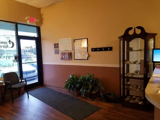 A waiting room with an entrance door, a cabinet with items, a plant, and a reception desk.