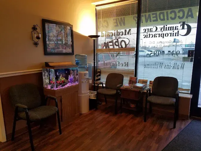 A chiropractic clinic waiting room with chairs, an aquarium, water cooler, and window.