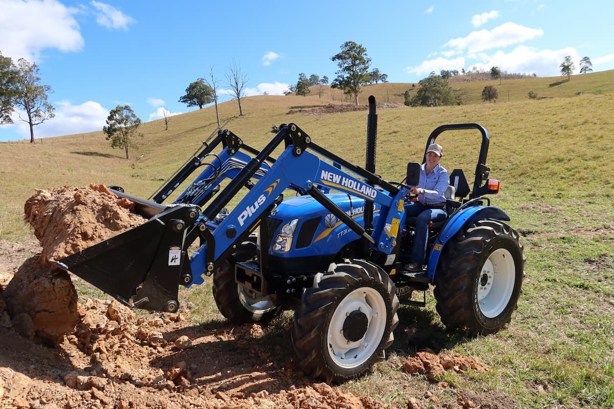 A Man Is Driving a Blue Tractor in A Field — Cheshire Machinery in Murgon, QLD