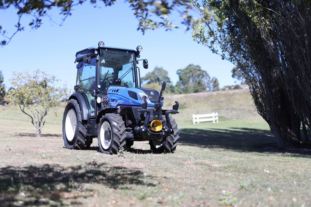 A Blue Tractor Is Parked in A Grassy Field Next to A Tree — Cheshire Machinery in Svensson Heights, QLD