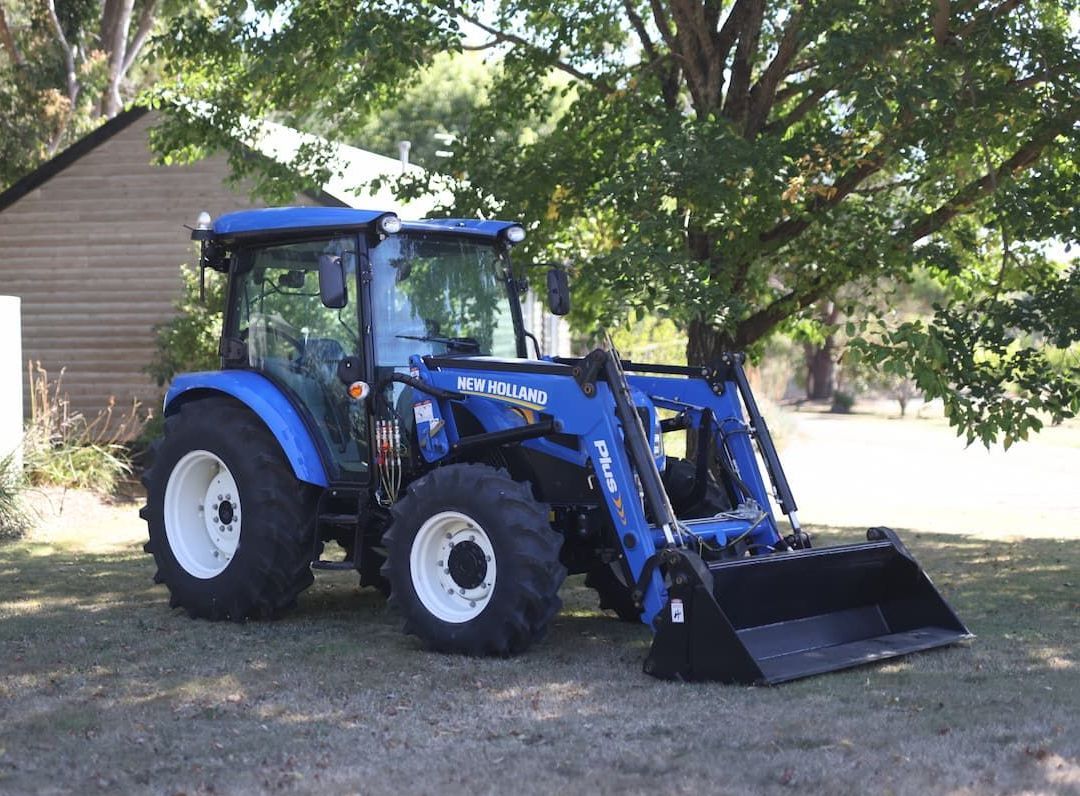 A Blue Tractor with A Bucket Attached to It Is Parked in A Yard — Cheshire Machinery in Svensson Heights, QLD