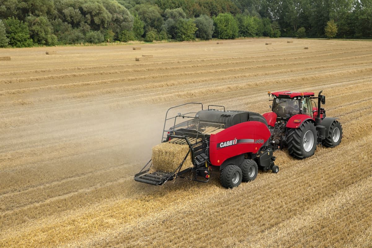 A Red Tractor Is Baling Hay in A Field — Cheshire Machinery in Murgon, QLD