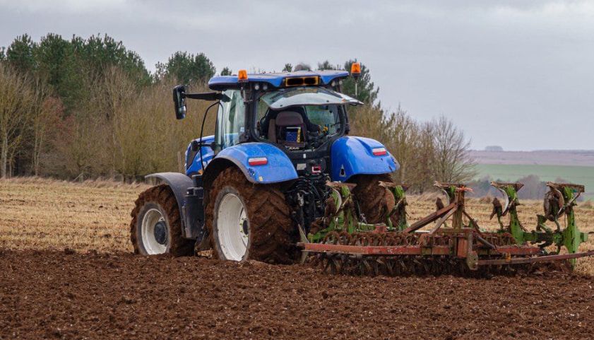 A Blue Tractor Is Parked in A Grassy Field Next to A Tree — Cheshire Machinery in Murgon, QLD