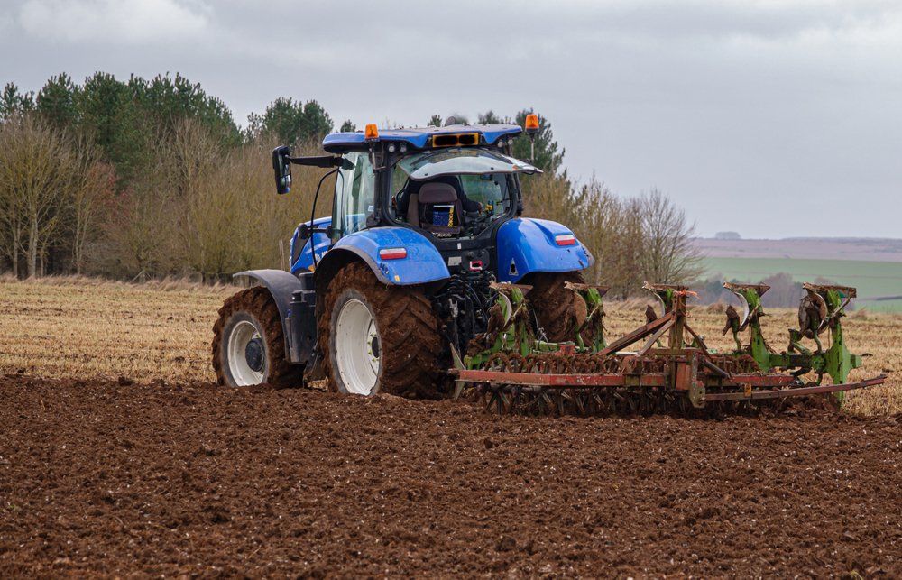 A Blue Tractor Is Plowing a Field with A Plow — Cheshire Machinery in Svensson Heights, QLD