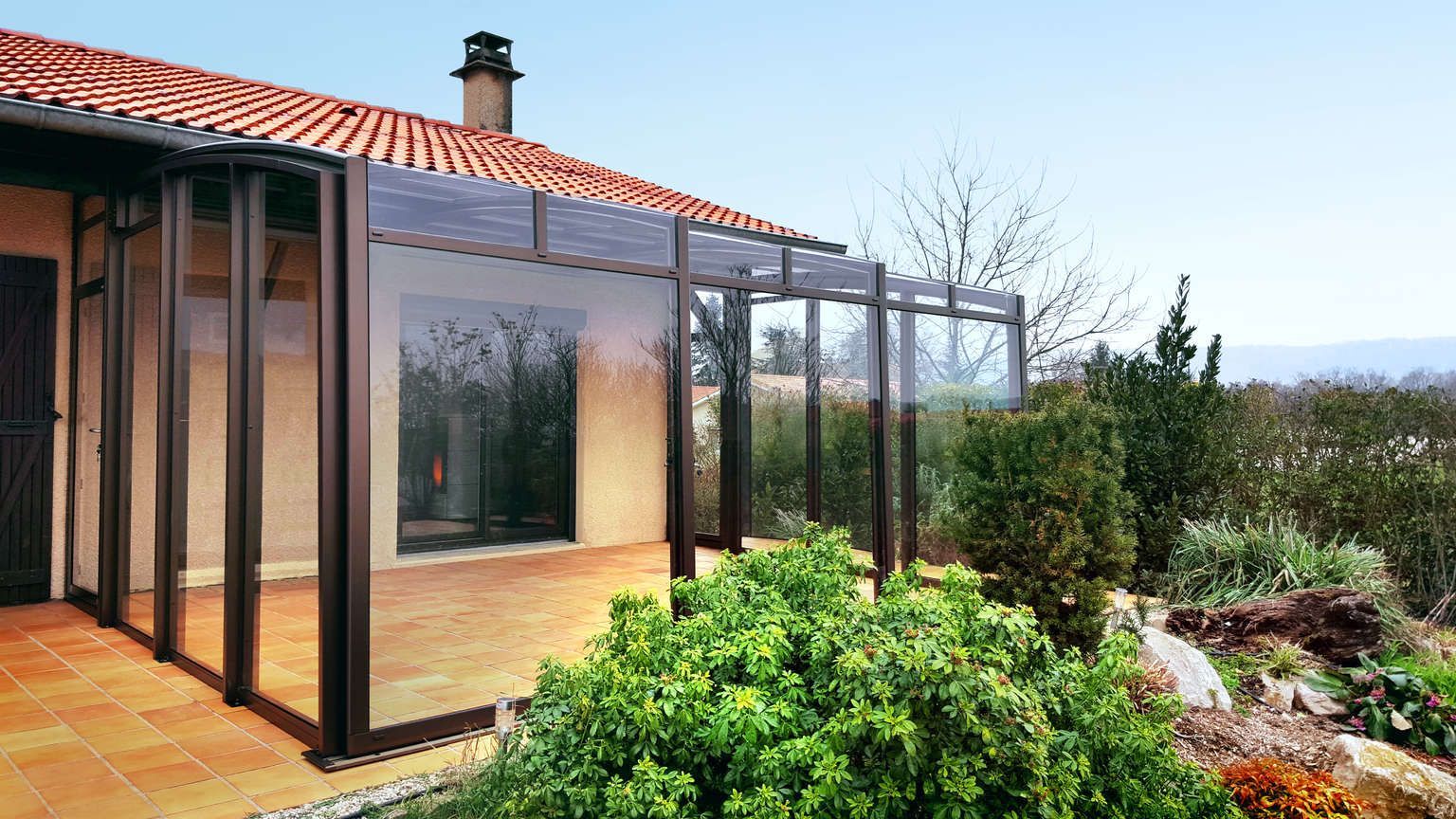 Ein Haus mit einer großen Glasveranda und einem roten Ziegeldach.