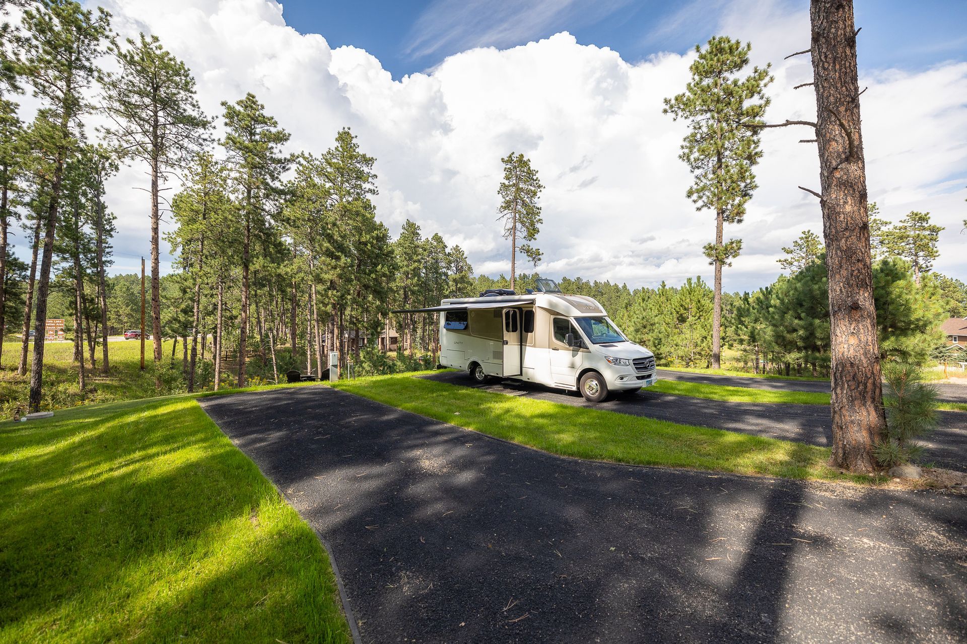 A white rv is parked in a grassy area surrounded by trees.