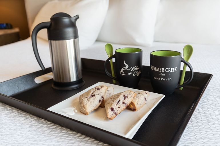 A tray with a plate of cookies , two mugs and a thermos on a bed.