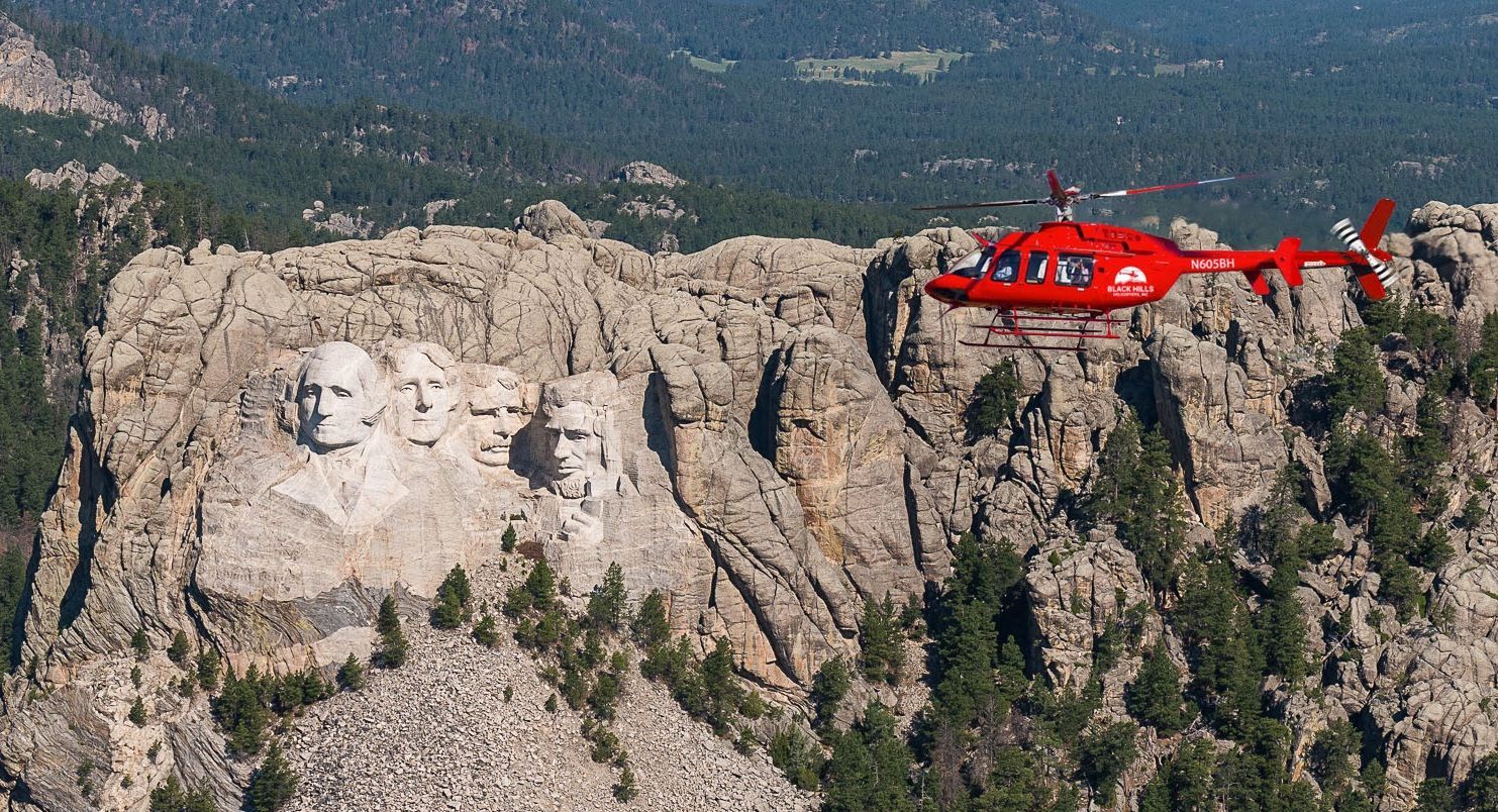 A red helicopter is flying over a mountain.