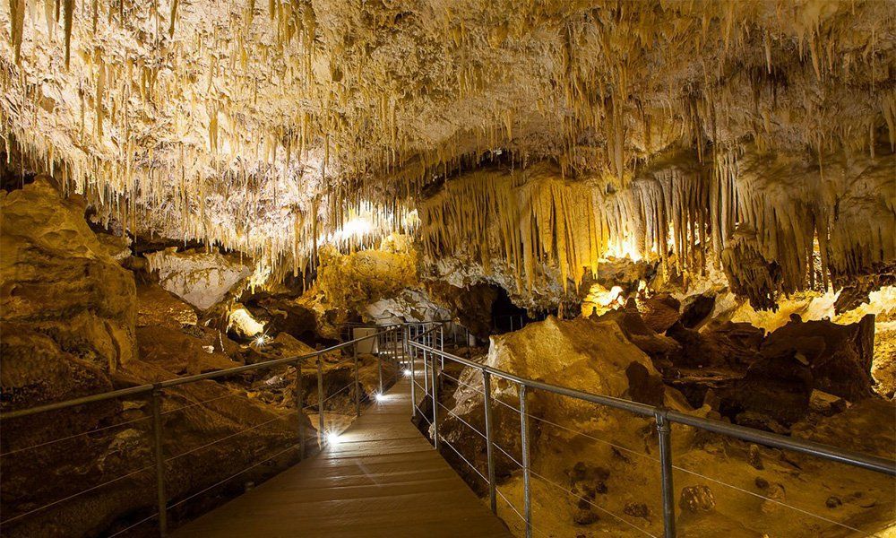 A person is walking through a cave with icicles hanging from the ceiling.