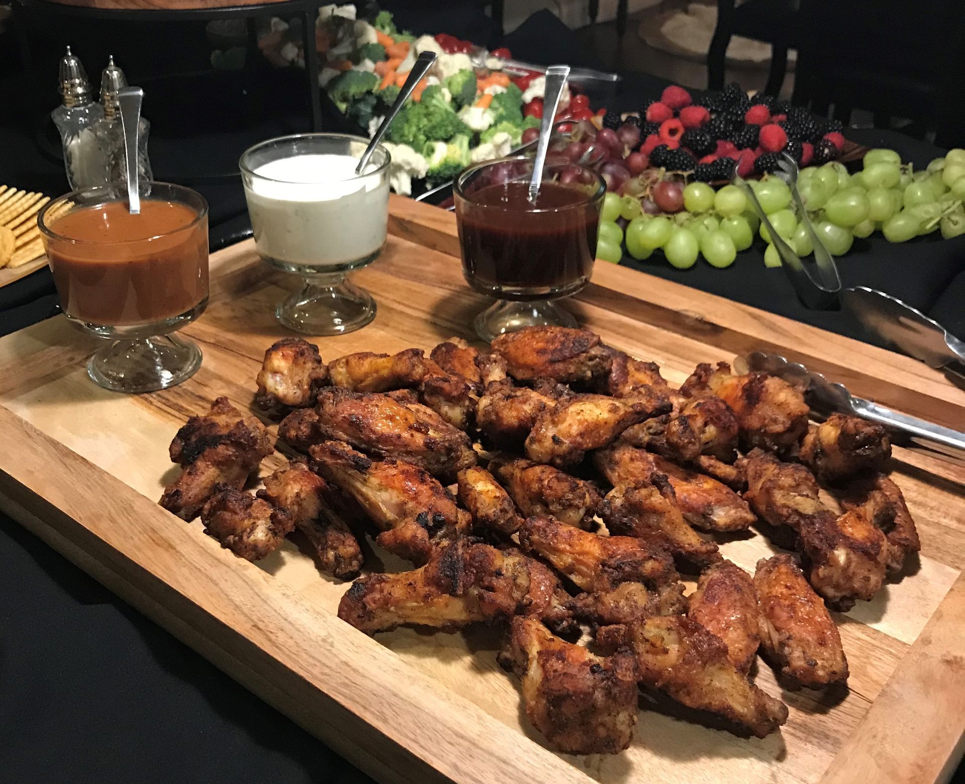 A wooden cutting board topped with chicken wings and dipping sauces.