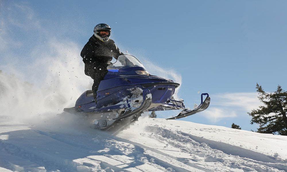 A man is riding a snowmobile down a snowy hill.