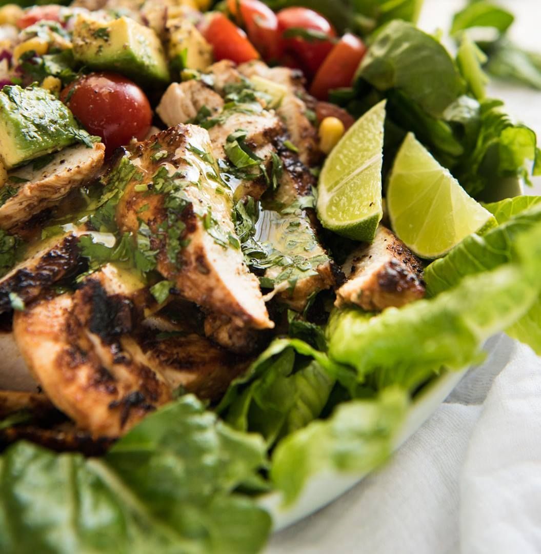 A salad with chicken , lettuce , tomatoes and limes on a plate