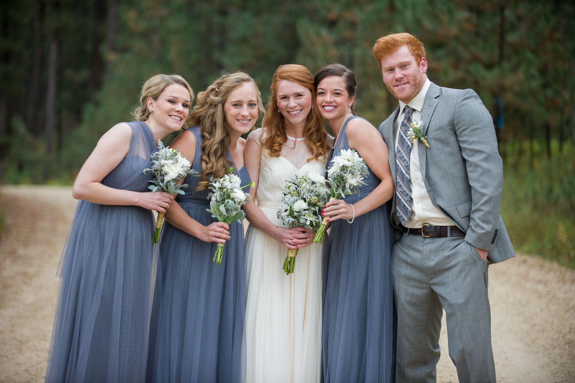 A bride and her bridesmaids are posing for a picture on a dirt road.