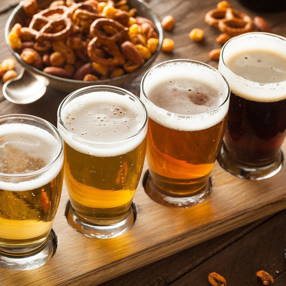 Four glasses of beer are lined up on a wooden tray.