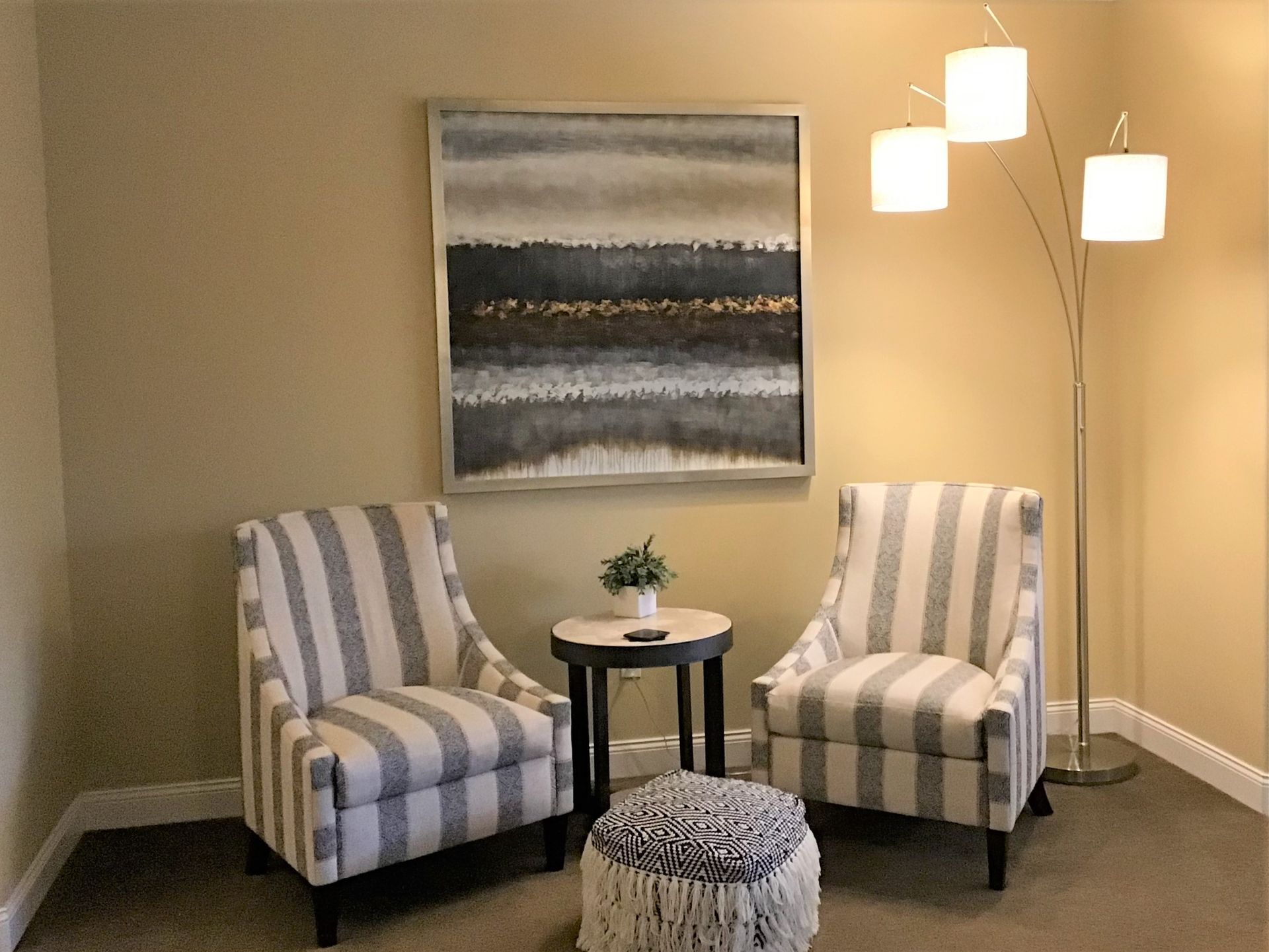 A living room with two chairs , a table and a painting on the wall.