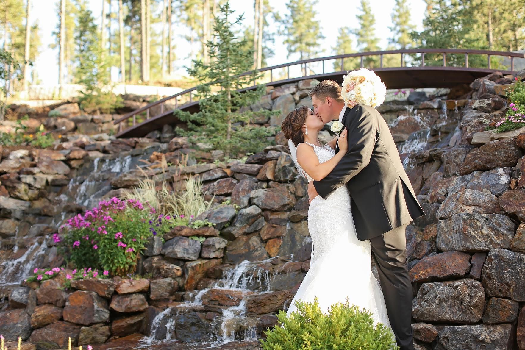 A bride and groom are kissing in front of a waterfall.