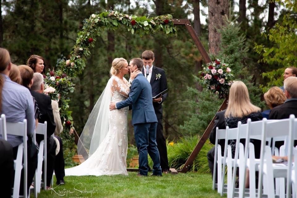 A bride and groom are kissing during their wedding ceremony while their guests watch.