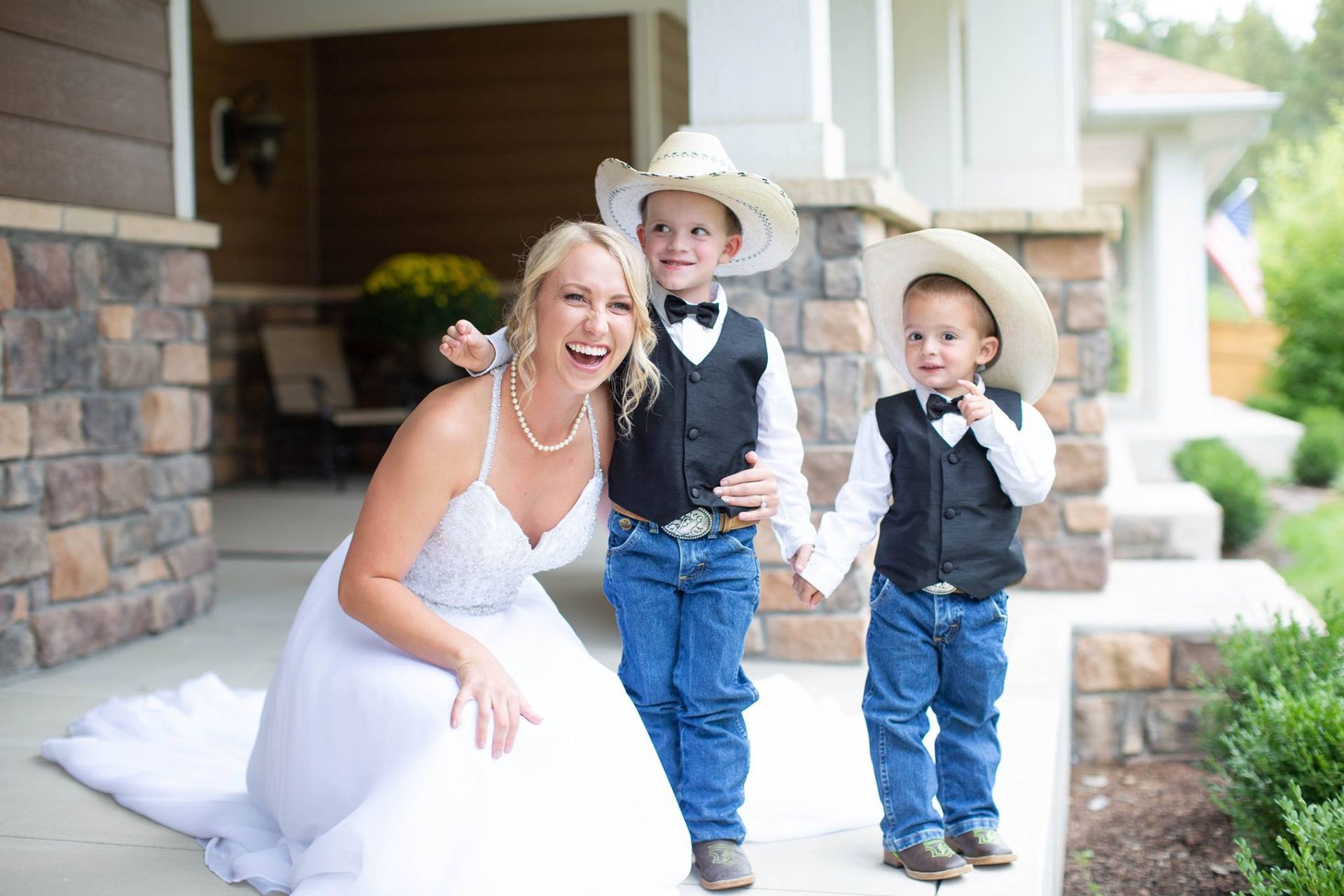 A bride and two groomsmen are posing for a picture in front of a house.