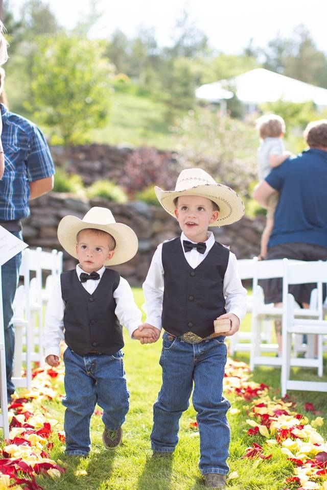 Two little boys wearing cowboy hats and bow ties are walking down the aisle at a wedding.