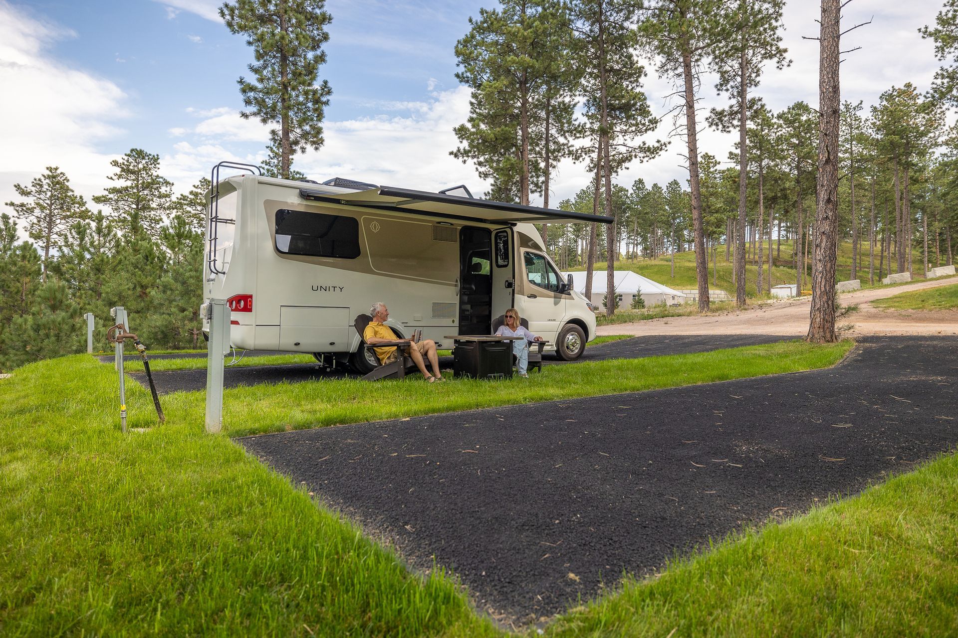 A couple is sitting on a bench in front of a rv parked in a grassy area.
