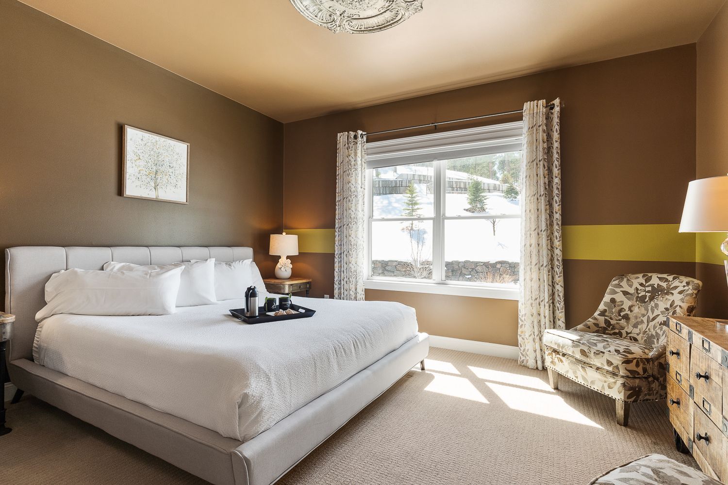 A bedroom with a large bed , chair , dresser and window.