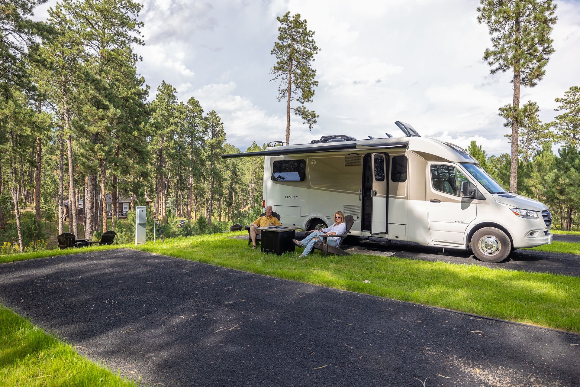 A couple is sitting in front of a rv parked on the side of a road.