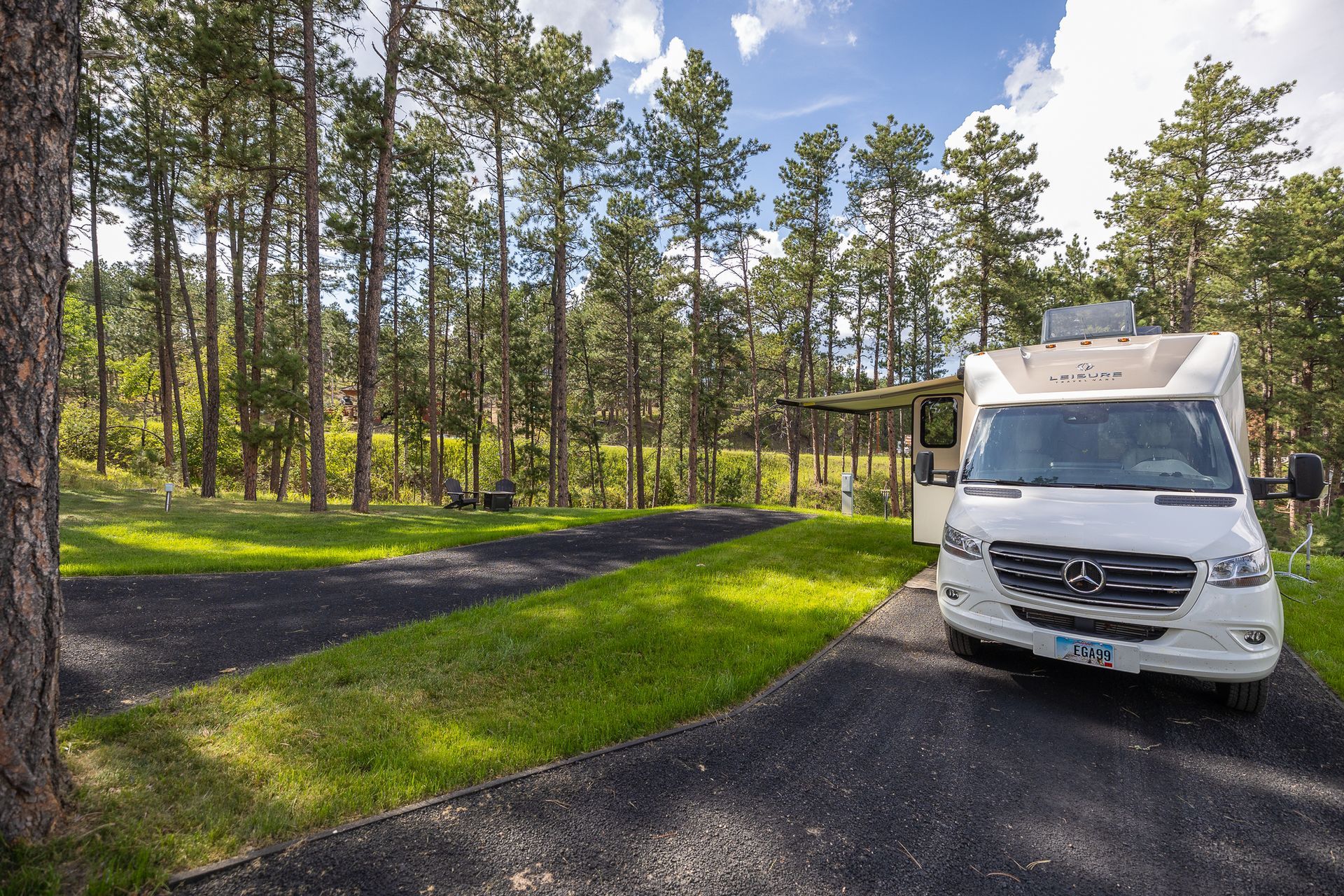 A white rv is parked on a dirt road in the middle of a forest.