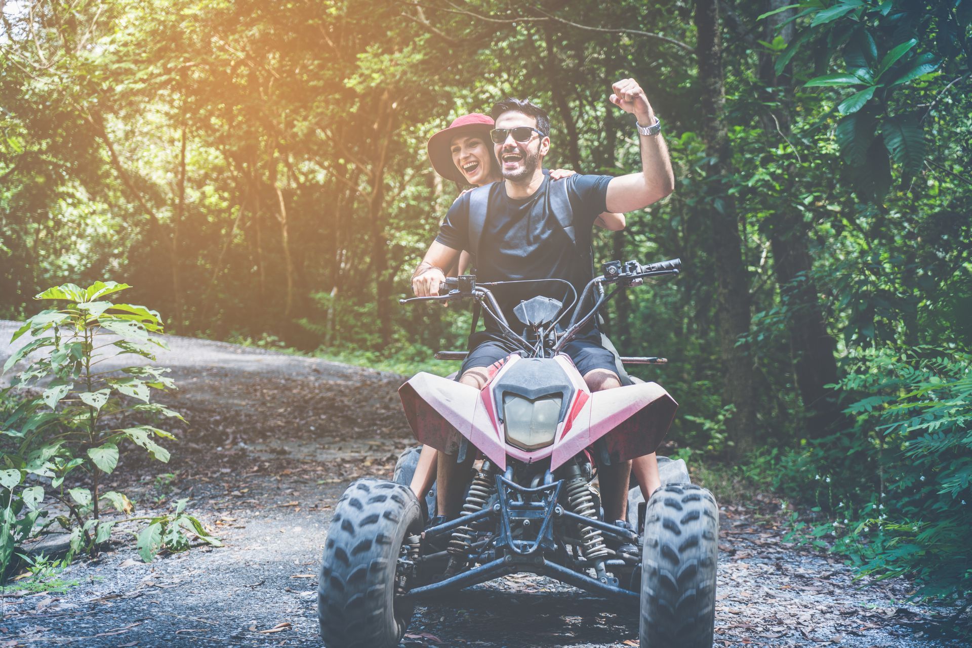 A man and a woman are riding an atv in the woods.