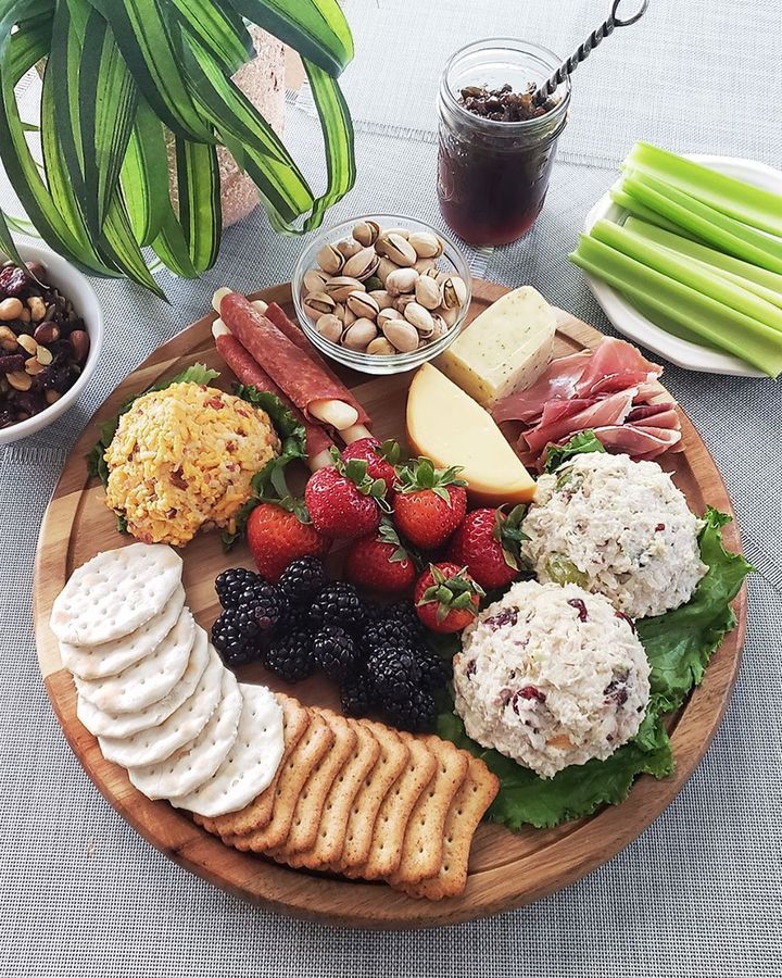 A wooden cutting board topped with crackers , fruit , cheese and nuts.