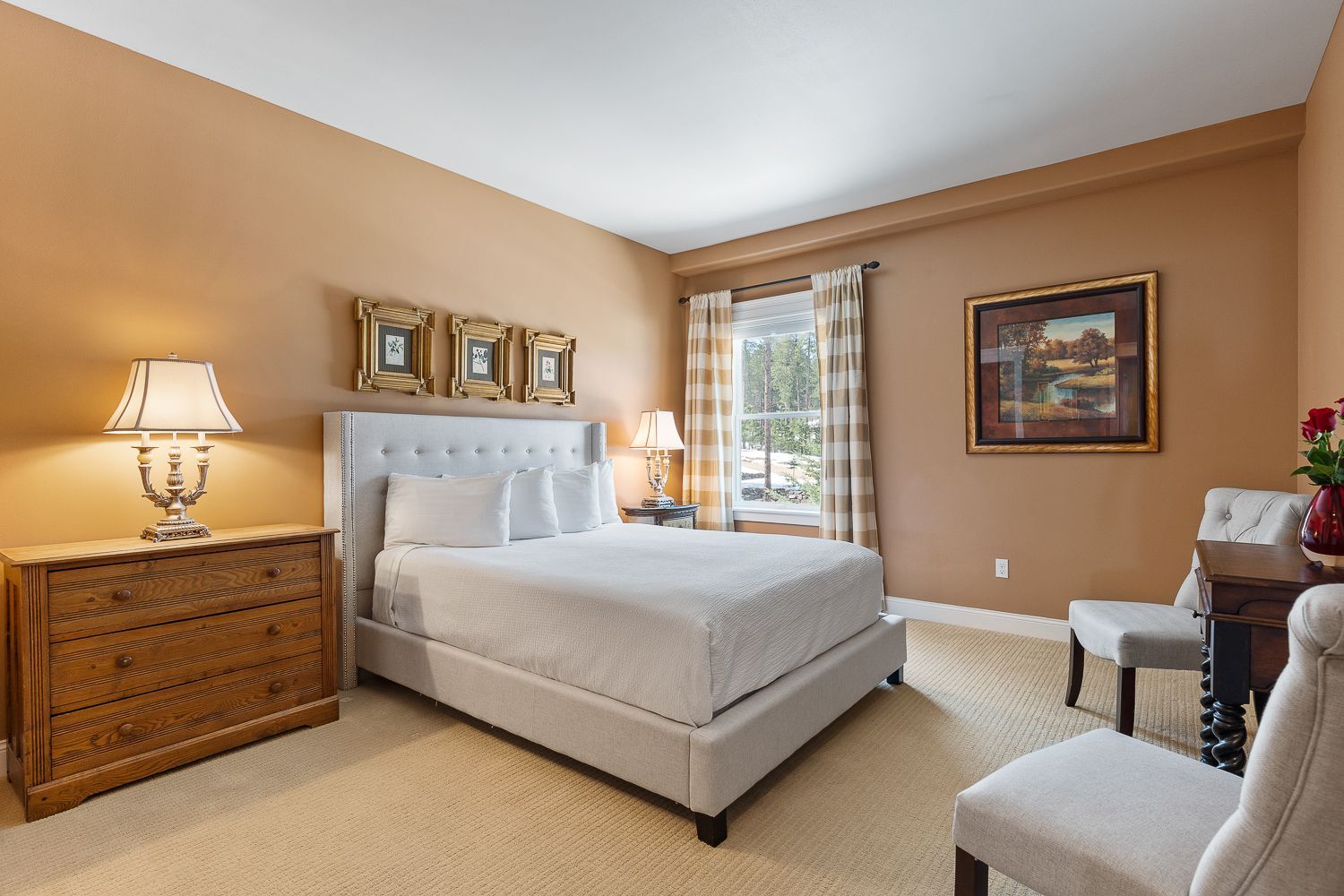 A bedroom with a large bed , dresser , chairs and lamps.