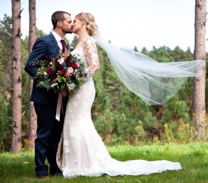A bride and groom are kissing in front of a forest.