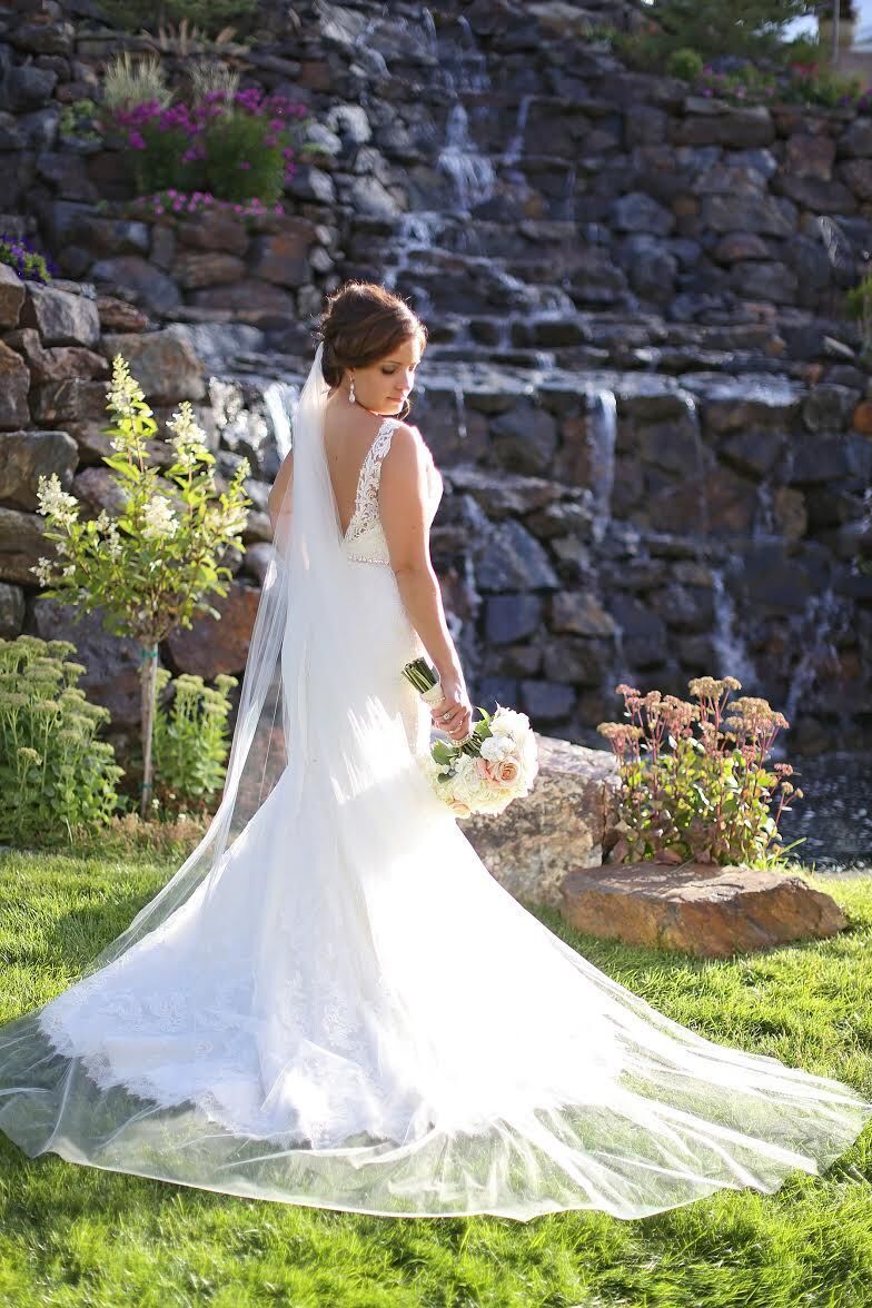 A bride in a wedding dress is standing in front of a waterfall.