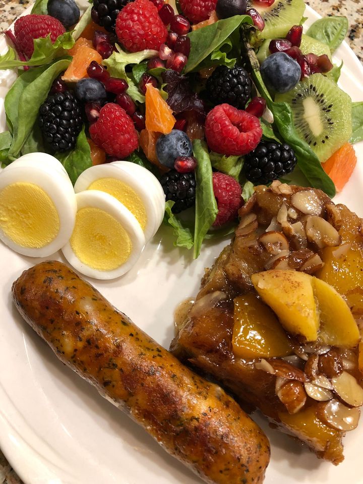 A white plate topped with a sausage , eggs , fruit and a salad.
