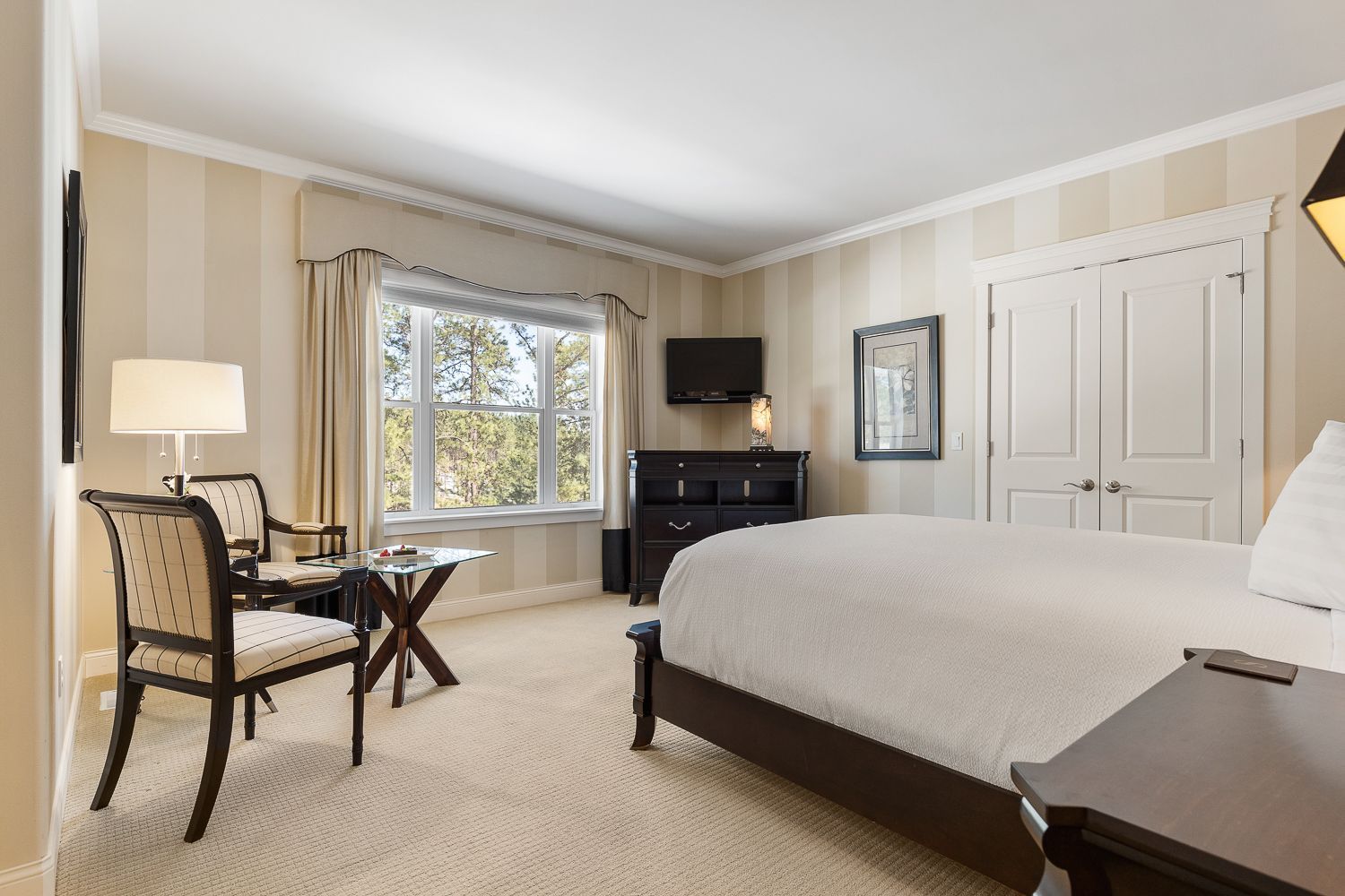A hotel room with a king size bed , chairs , table and television.