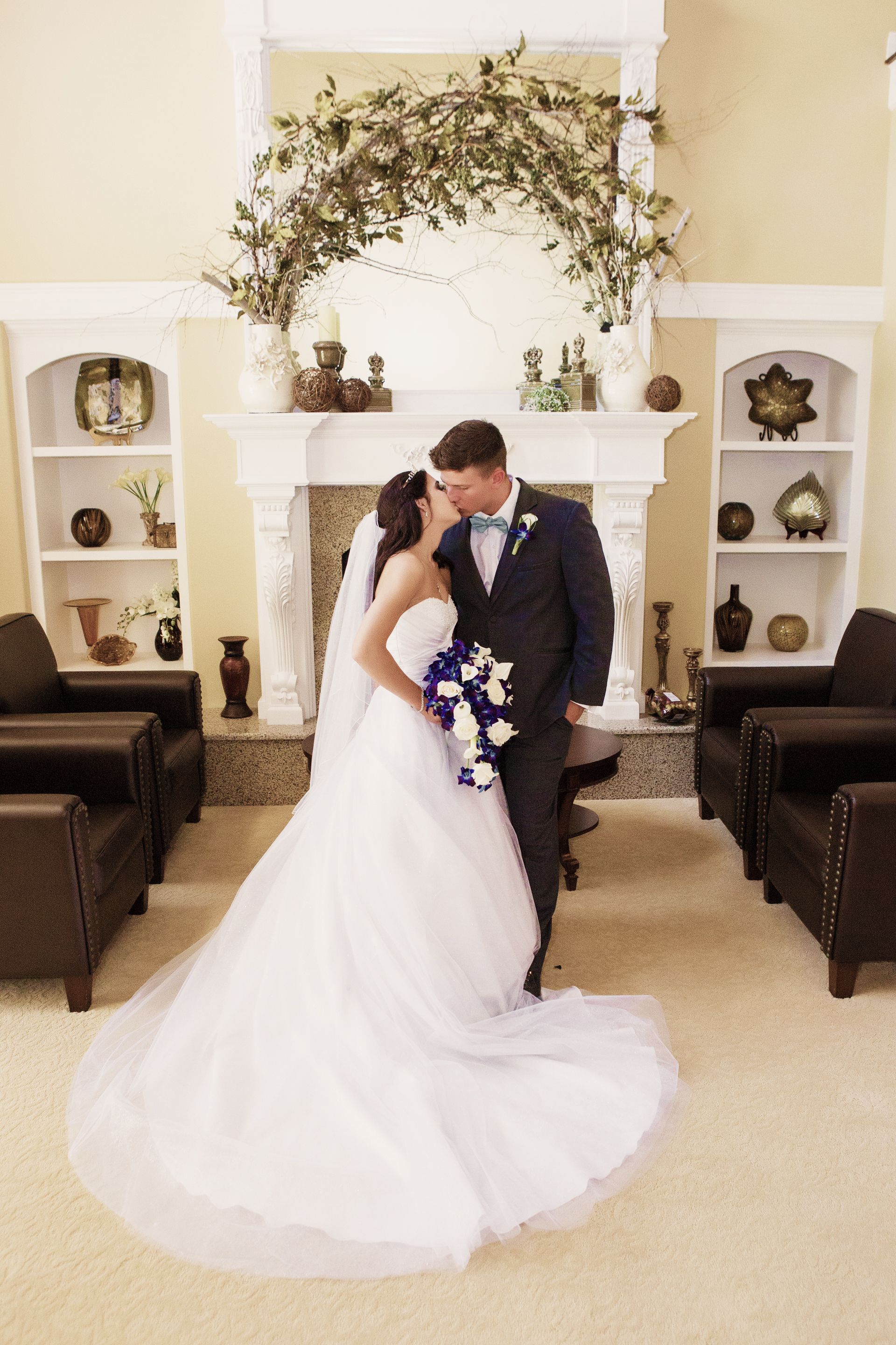 A bride and groom are kissing in front of a fireplace.