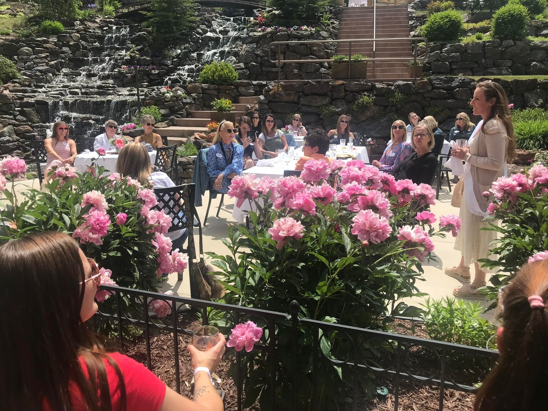 A group of people are sitting at tables in a garden with pink flowers.