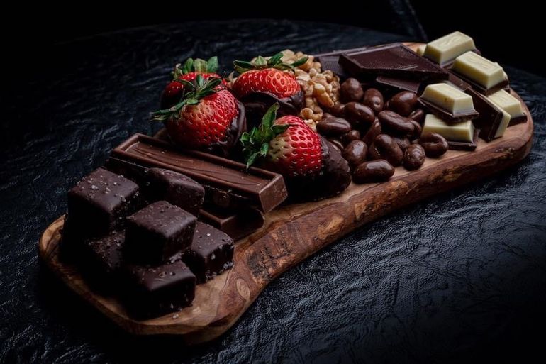 A wooden cutting board topped with chocolate , strawberries and nuts.