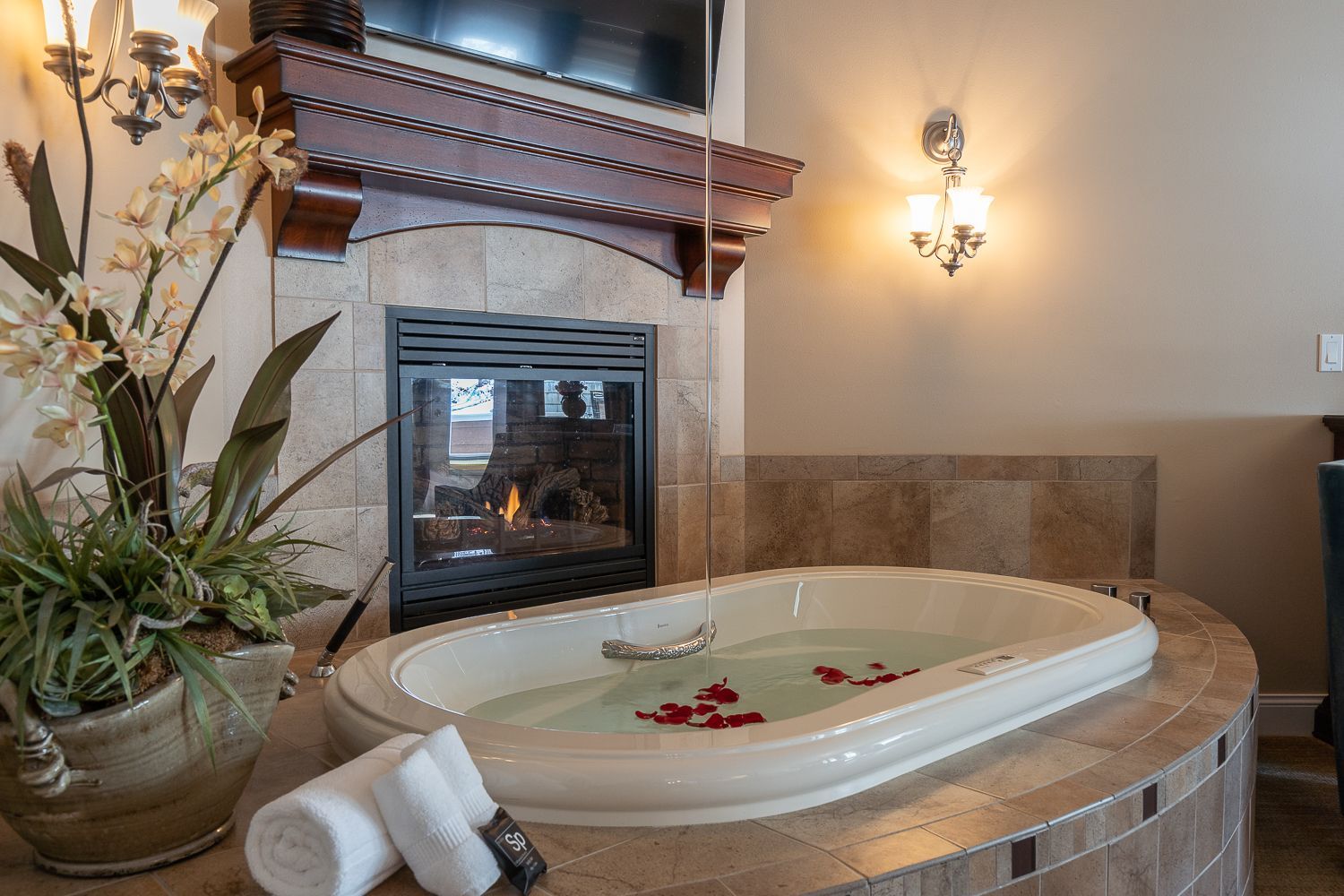 A jacuzzi tub filled with water and rose petals next to a fireplace.