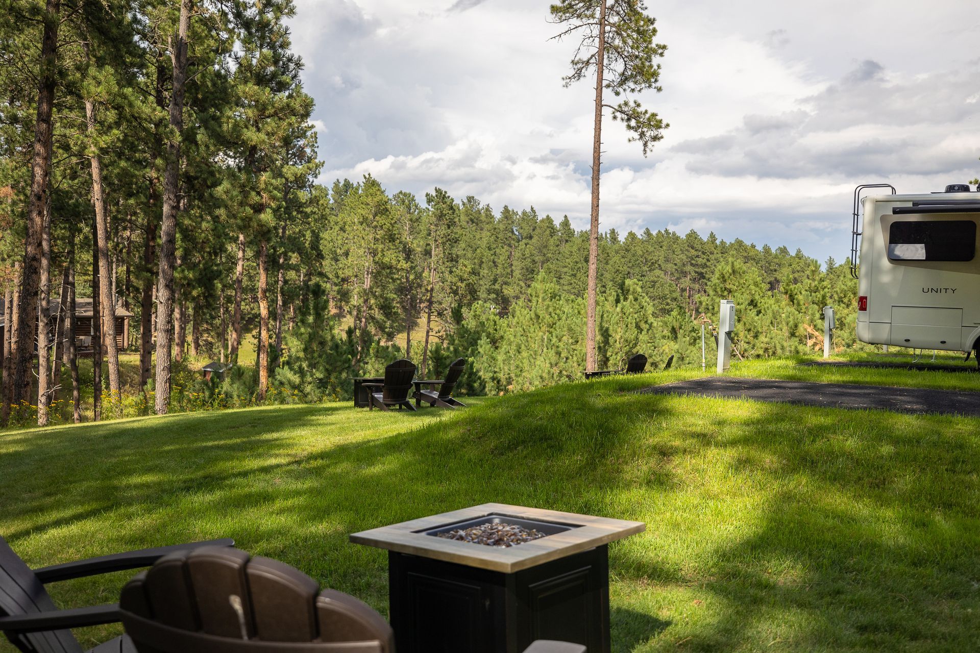 A fire pit in the middle of a lush green field with a rv in the background.