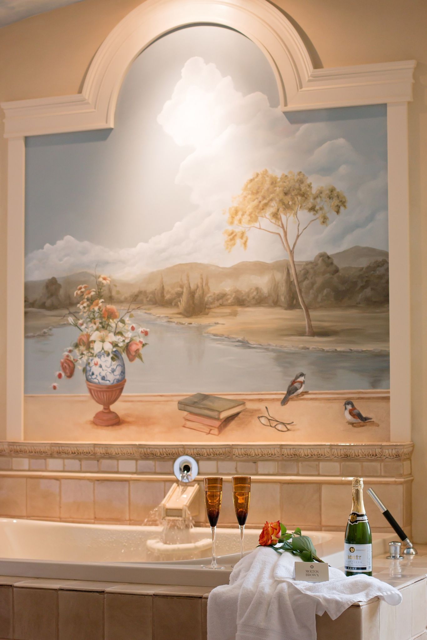 A bathroom with a large painting on the wall above the bathtub.
