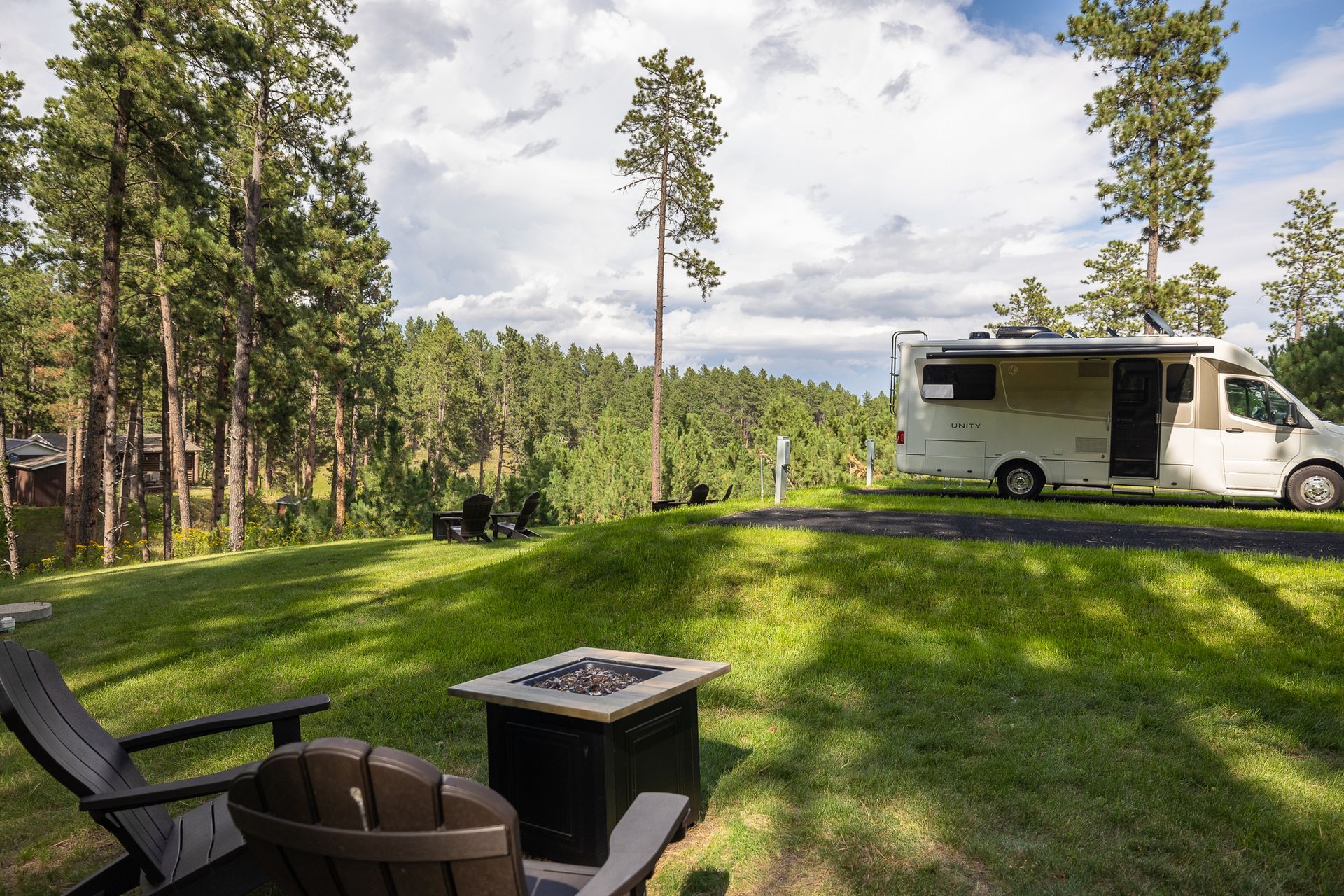 A rv is parked in a grassy field next to a fire pit.