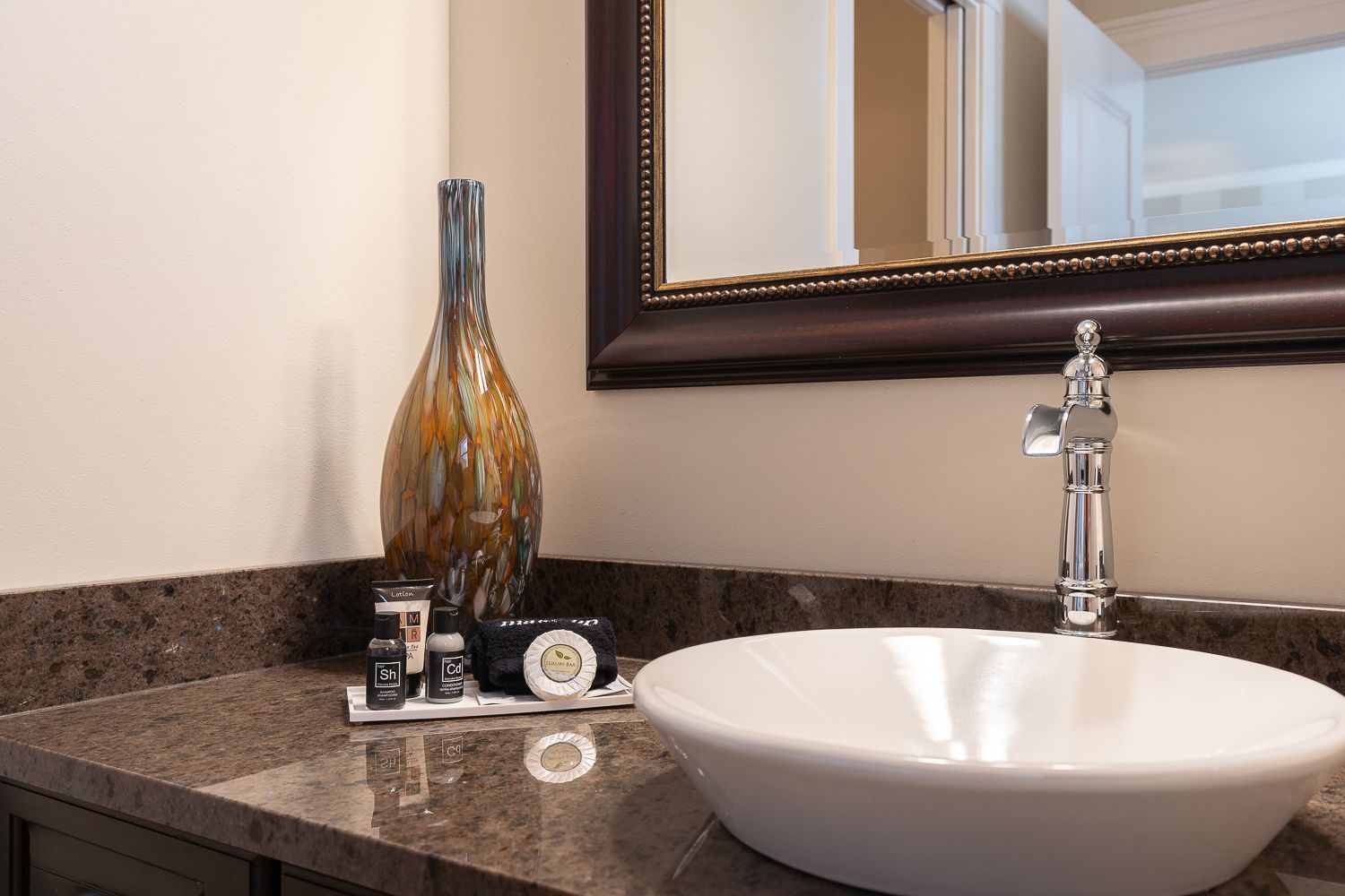 A bathroom with a sink , mirror and vase on the counter.